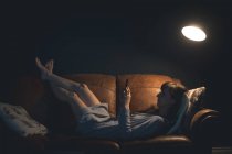 Mulher usando telefone celular enquanto deitado no sofá na sala de estar — Fotografia de Stock
