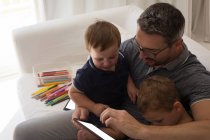 Батько з синами, використовуючи цифровий планшет у вітальні вдома — стокове фото