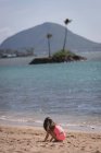Vue latérale de la fille d'âge élémentaire jouant dans le sable à la plage — Photo de stock