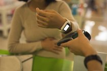 Mujer embarazada haciendo el pago a través de smartwatch en la tienda - foto de stock