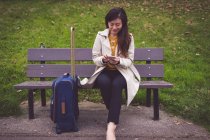 Donna d'affari sorridente utilizzando il telefono cellulare mentre seduto sulla panchina — Foto stock