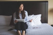 Empresária segurando documentos enquanto usa tablet digital na cama no quarto do hotel — Fotografia de Stock