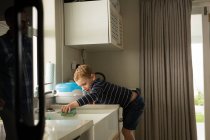 Мальчик убирает раковину на кухне дома — стоковое фото