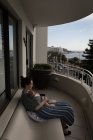 Junge Mutter sitzt auf Bank und trägt ihr Baby im Tragetuch auf dem Balkon an einem sonnigen Tag — Stockfoto