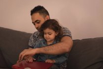 Padre e hija usando el ordenador portátil en la sala de estar en casa . - foto de stock