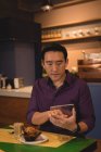 Asian man using digital tablet while sitting in coffee shop — Stock Photo