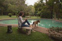 Mujer y su perro mascota relajándose cerca de la piscina en el patio trasero - foto de stock
