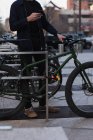 Человек, стоящий рядом с велосипедом и использующий мобильный телефон на улице — стоковое фото