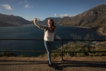 Smiling woman taking selfie at observation point in sunlight — Stock Photo