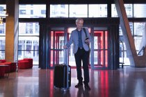 Geschäftsmann benutzt Handy beim Betreten des Hotels mit Gepäck — Stockfoto