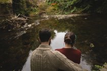 Visão traseira do casal sentado à beira do rio — Fotografia de Stock