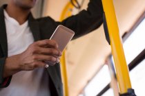 Mid section of businessman holding mobile phone while travelling in bus — Stock Photo