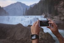 Крупним планом чоловік фотографії водоспаду з мобільним телефоном — стокове фото
