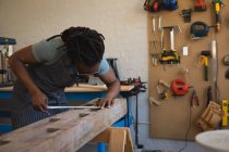 Плотник измеряет деревянную доску с рулеткой в мастерской — стоковое фото