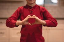 Хлопчик формує форму серця руками вдома — стокове фото