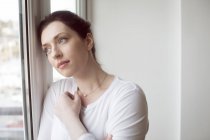 Thoughtful woman standing near window at home. — Stock Photo