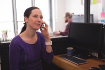 Female executive talking on mobile phone at desk in office — Stock Photo