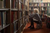 Молодая женщина снимает книгу с книжной полки в библиотеке — стоковое фото