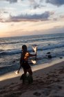 Homme danseur de feu performant avec des bâtons de levi de feu à la plage au crépuscule — Photo de stock