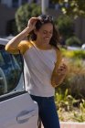 Молодая женщина с помощью мобильного телефона, стоя рядом с электромобилем — стоковое фото