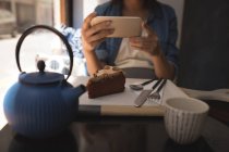Femme enceinte prenant des photos de pâtisserie avec téléphone portable au café — Photo de stock