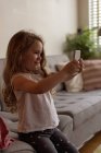 Милая девушка делает селфи с мобильного телефона в гостиной на дому — стоковое фото