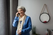 Старшая женщина разговаривает по мобильному телефону дома — стоковое фото
