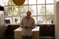 Hombre mayor usando el teléfono móvil en la cocina en casa - foto de stock