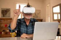 Homem sênior usando fone de ouvido realidade virtual com laptop na cozinha em casa — Fotografia de Stock
