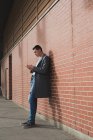 Человек с помощью мобильного телефона, опираясь на стену в коридоре — стоковое фото