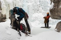 Hombre escalador chequeando mochila cerca de montaña de hielo rocoso - foto de stock