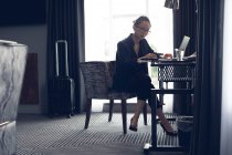 Mujer usando portátil en la mesa en la habitación de hotel - foto de stock