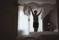Jovem mulher espalhando lençol sobre a cama no quarto em casa — Fotografia de Stock