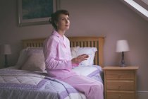 Femme réfléchie tenant tablette numérique sur le lit dans la chambre — Photo de stock