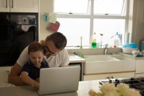 Father and son using laptop in kitchen at home — Stock Photo