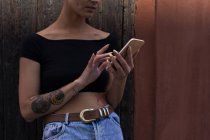 Середина молодої дорослої жінки, яка використовує мобільний телефон перед дерев'яною стіною . — стокове фото