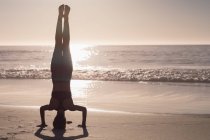 Donna in forma esibendosi headstand in spiaggia al tramonto . — Foto stock