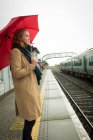 Young woman standing with umbrella at railway station — Stock Photo