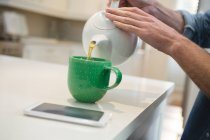 Sección media del hombre vertiendo té de limón en la taza en casa - foto de stock