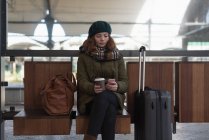 Donna con tazza di caffè utilizzando il telefono cellulare in sala d'attesa — Foto stock