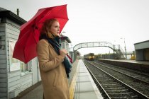 Junge Frau steht mit Regenschirm am Bahnhof — Stockfoto