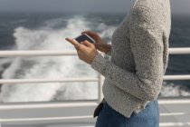 Средняя часть женщины, использующая мобильный телефон на круизном лайнере — стоковое фото