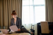 Ділова жінка дивиться документи на ліжко в готельному номері — стокове фото