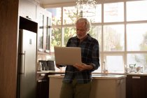 Uomo anziano utilizzando il computer portatile in cucina a casa — Foto stock