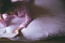 Frau benutzt digitales Tablet, während sie zu Hause im Schlafzimmer auf dem Bett liegt — Stockfoto