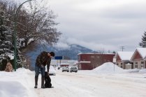 Mann streichelt Hund auf verschneiter Straße. — Stockfoto