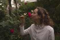 Вид сбоку на пахнущую красной розой женщину в саду — стоковое фото