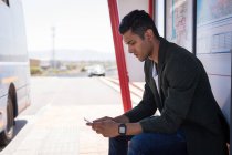 Joven hombre de negocios usando el teléfono móvil en la parada de autobús - foto de stock