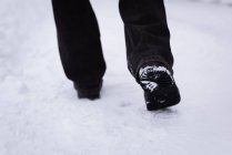 Baixa seção de homem andando na estrada coberta de neve . — Fotografia de Stock