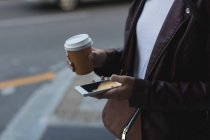 Media sezione di donna che utilizza il telefono cellulare mentre prende un caffè in strada — Foto stock